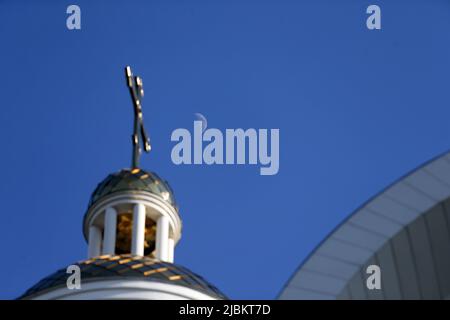 BUCHA, UKRAINE - le 6 JUIN 2022 - Une lune en croissant cirant est photographiée dans le ciel bleu au-dessus des dômes de l'église Saint Andrew le premier-appelé Apost Banque D'Images