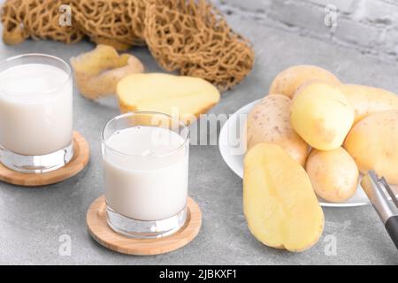 Lait de pomme de terre vegan en deux verres et tubercules de pomme de terre sur fond de table en pierre grise. Remplacement de lait alternatif à base de plantes et sans lactose, HEAL tendance Banque D'Images