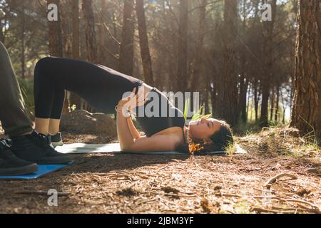 Jolie jeune fille faisant du yoga s'étire sur son tapis au coucher du soleil dans une forêt entourée d'arbres. Banque D'Images