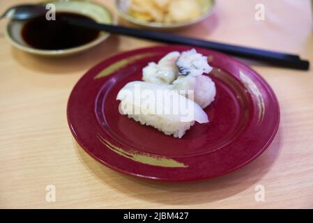 IKA nigiri sushi ou sushi calmar frais, sushi calmar sur un plat rouge avec des baguettes d'image floues, sauce soja ou shoyu et gingembre. Banque D'Images