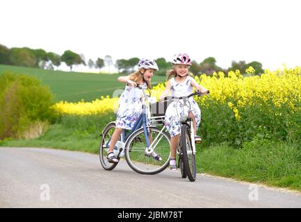 Les sœurs jumelles sont vues à vélo dans la campagne. Ils ont un visage souriant heureux sur eux comme ils aiment leur tour en vélo en plein air. Banque D'Images