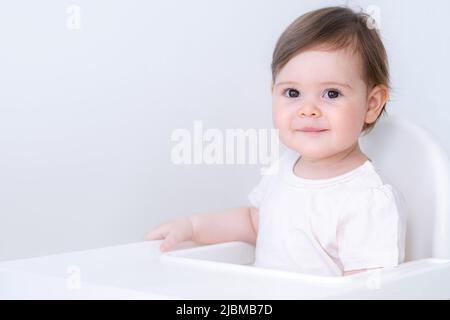 Portrait mignon bébé fille sur la cuisine assis sur une chaise haute, sourire enfant heureux de manger la première nourriture solide Banque D'Images