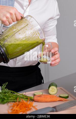 Homme méconnaissable qui prépare du smoothie maison vert au mélangeur et verse sur un verre. Concept de mode de vie sain. Banque D'Images