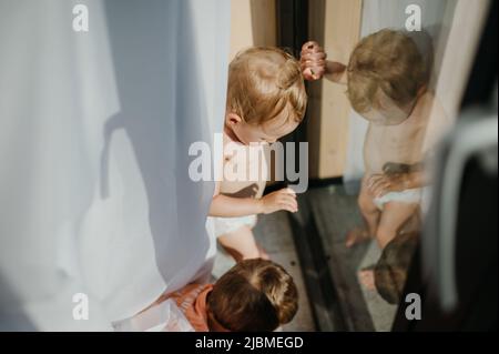 Mignon bébé fille et garçon jouant, se cachant derrière des rideaux à la maison. Banque D'Images