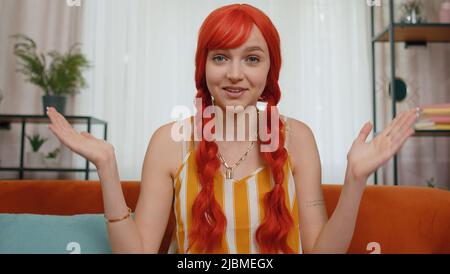 POV de la jeune femme à tête rouge assis sur un canapé, regardant la caméra, faisant la vidéo webcam conférence téléphonique avec des amis ou des parents, appréciant la conversation agréable. Fille riant, saluant seul à la maison Banque D'Images