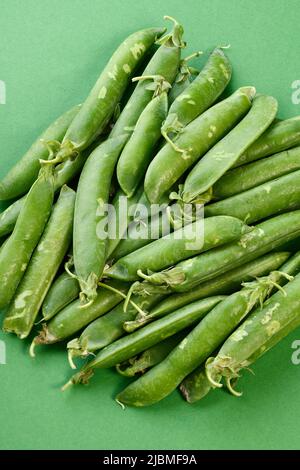 Une pile de petits pois dans des gousses sur fond vert Banque D'Images