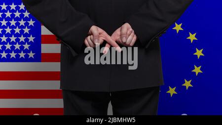 Homme debout avec les doigts croisés contre le fond des drapeaux des États-Unis et de l'Union européenne Banque D'Images