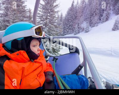 Un petit garçon s'assoit dans le télésiège de ski de la station de sports alpins Banque D'Images