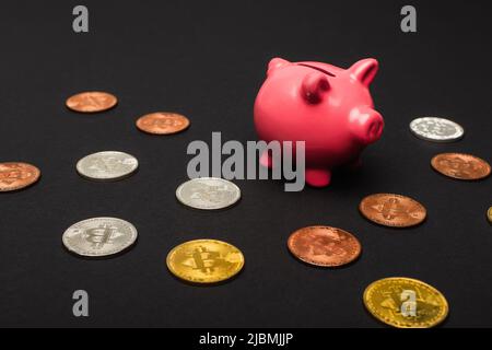 KIEV, UKRAINE - 26 AVRIL 2022 : différentes pièces de crypto près de la banque de porc sur fond noir Banque D'Images