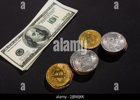 KIEV, UKRAINE - 26 AVRIL 2022 : vue en grand angle des billets en dollars près des bitcoins d'or et d'argent sur fond noir Banque D'Images