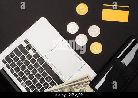 KIEV, UKRAINE - 26 AVRIL 2022: Vue de dessus des dollars près de la carte de crédit avec ordinateur portable et bitcoins sur fond noir Banque D'Images