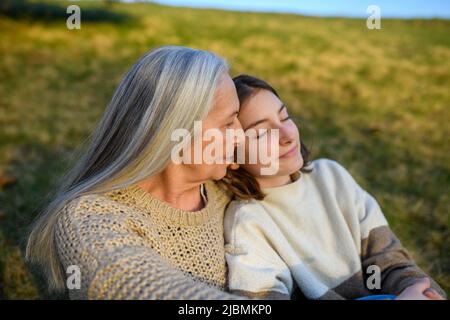 Une grand-mère âgée heureuse avec un grand-daguhter adolescent qui s'enserre dans la nature le jour du printemps. Banque D'Images