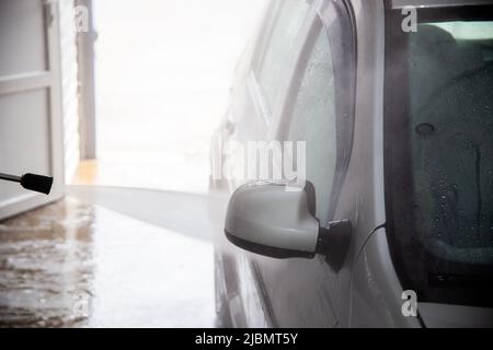 Un procédé de rinçage du savon sud sur le miroir de voiture argenté avec un jet d'eau sous pression au poste de lavage de voiture intérieur libre-service Banque D'Images