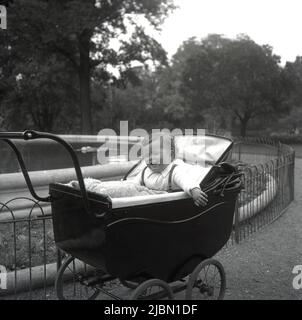 1950s, historique, à l'extérieur d'un parc sur un chemin à côté d'une fontaine, un bébé garçon assis dans un pram traditionnel construit en autocar ou babycalèche de l'époque, Margate, Kent, Angleterre, Royaume-Uni. Banque D'Images