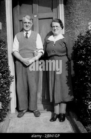 1950s, historique, un couple âgé marié debout ensemble à l'extérieur de la porte de leur maison, Angleterre, Royaume-Uni. Banque D'Images