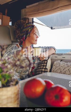 Une femme adulte sereine admirant une destination à l'extérieur, assise à l'intérieur de son camping-car moderne et prenant un café. Voyageur indépendant touriste femme peopl Banque D'Images