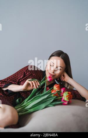 Bonne femme appréciez le bouquet de tulipes. Femme de ménage appréciant un bouquet de fleurs tout en se relaxant sur un sac de haricots confortable. Maison agréable. Anti-allergie Banque D'Images