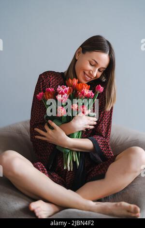 Bonne femme appréciez le bouquet de tulipes. Femme de ménage appréciant un bouquet de fleurs tout en se relaxant sur un sac de haricots confortable. Maison agréable. Anti-allergie Banque D'Images