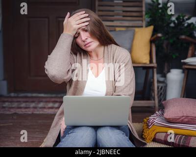 Femme âgée d'âge moyen stressée et oubliée souffrant de maux de tête après un travail informatique. Une dame fatiguée contrariée se sentant stress, fatigue ou migraine en utilisant un ordinateur portable au bureau à domicile. Banque D'Images