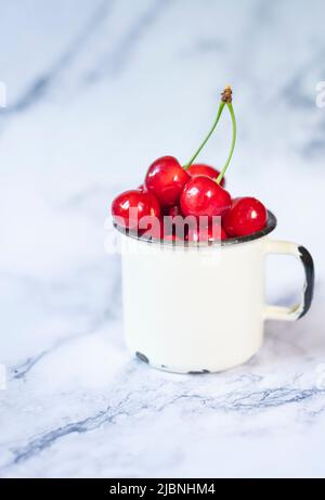 cerises fraîchement cueillies dans une tasse en métal sur une table en céramique Banque D'Images