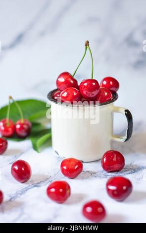 cerises fraîchement cueillies dans une tasse en métal sur une table en céramique Banque D'Images