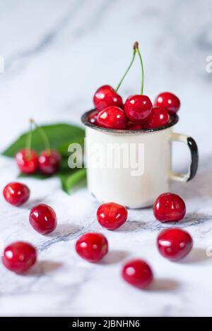 cerises fraîchement cueillies dans une tasse en métal sur une table en céramique Banque D'Images