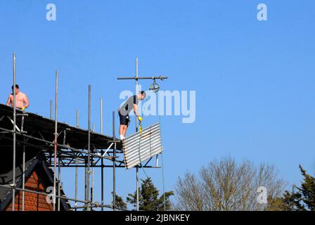 Deux hommes retirant des feuilles de fonte ondulée de la couverture temporaire de toit sur la nouvelle maison Banque D'Images