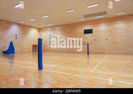 Filet de volley-ball dans une salle de sport vide avec un panier de basket-ball mobile en arrière-plan Banque D'Images