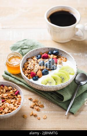 Petit déjeuner sain avec une tasse de café et un bol de granola avec yaourt grec, myrtilles et kiwi sur une table en bois Banque D'Images