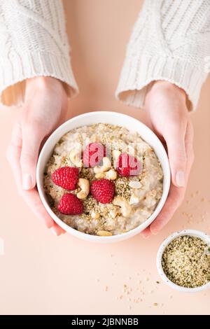 Bol de porridge de flocons d'avoine avec baies et noix dans les mains de la femme. Concept de régime végétalien sain, alimentation propre, perte de poids. Vue de dessus Banque D'Images