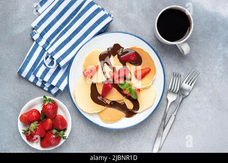 Crêpes ou crêpes aux fraises et au chocolat sur l'assiette servies avec une tasse de café noir, fond de table en béton gris. Vue de dessus Banque D'Images