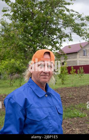 Fermier mâle mature dans une casquette sur le fond de la maison et du jardin. Agriculture et culture de plantes. Banque D'Images