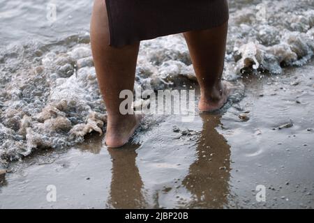 Courte peau foncée pieds nus femme jambes marchant à travers la côte de mer, plage, mousse de lavage. Personne multiculturelle, vacances d'été Banque D'Images