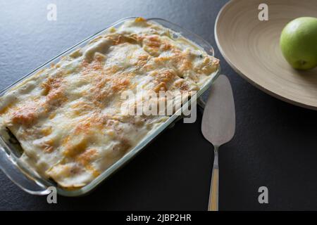 Plat de lasagnes maison sur un comptoir de cuisine noir. Pomme verte dans un bol, Banque D'Images