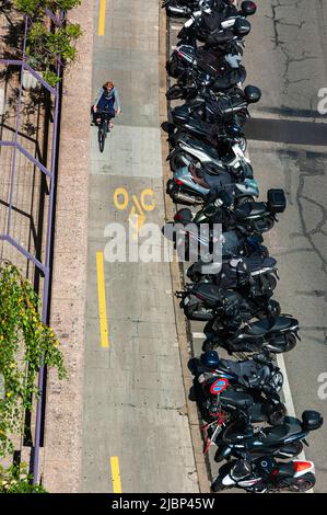 Genève, Suisse - 3 juin 2022 : le cycliste passe le long de la piste cyclable et passe devant une longue ligne de motos garées Banque D'Images