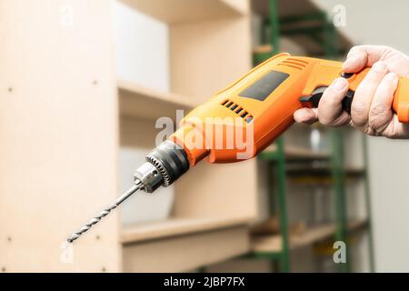 Homme tenant une perceuse orange avec un foret mural. Banque D'Images