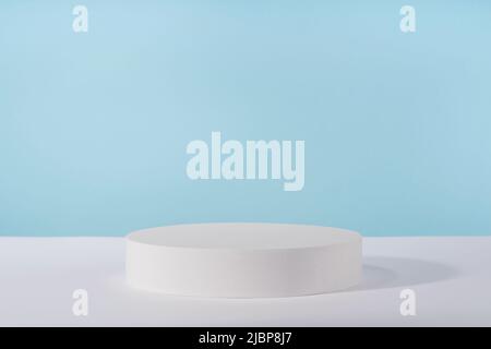 Piédestal pour l'emballage de produits cosmétiques sur fond bleu. Vitrine pour la présentation de bijoux, plate-forme blanche pour la publicité de parfum Banque D'Images