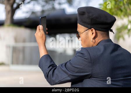 Latino gay homme avec maquillage sur le port de chapeau tendance regardant le téléphone cellulaire dans un parc Banque D'Images
