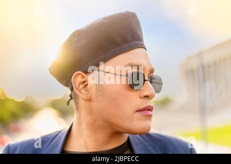 Latino gay mâle avec maquillage portant chapeau tendance, à côté du coucher du soleil Banque D'Images