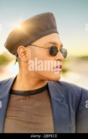 Latino gay mâle avec maquillage portant chapeau tendance, à côté du coucher du soleil Banque D'Images