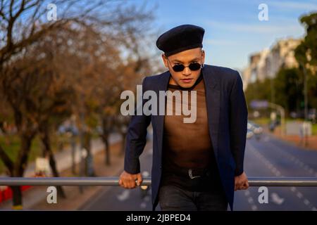 Latino gay mâle avec maquillage portant chapeau tendance posé sur un pont Banque D'Images