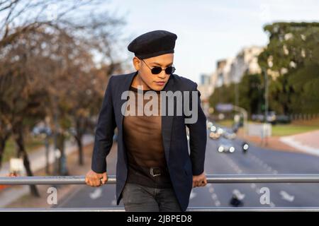 Latino gay mâle avec maquillage portant chapeau tendance posé sur un pont Banque D'Images