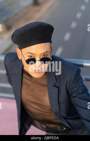 Latino gay mâle avec maquillage portant chapeau tendance posé sur un pont Banque D'Images
