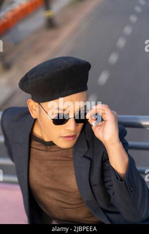 Latino gay mâle avec maquillage portant chapeau tendance posé sur un pont Banque D'Images