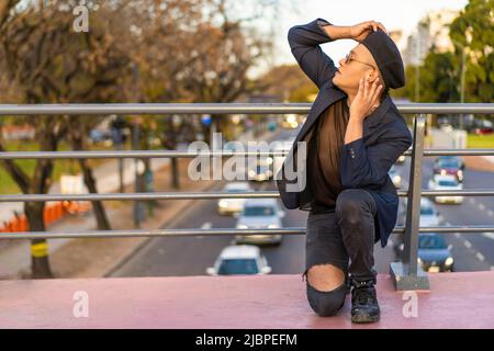 Latino gay mâle avec maquillage portant chapeau tendance posé sur un pont Banque D'Images