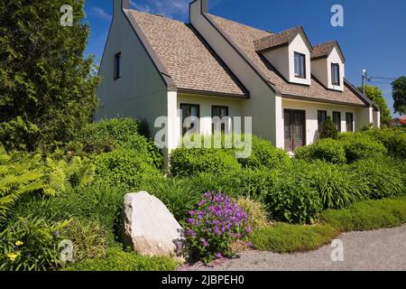 Maison de style cottage en stuc blanc et brun avec cour avant paysagée au printemps. Banque D'Images