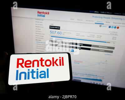 Personne tenant un téléphone portable avec le logo de la société britannique de services Rentokil initial plc à l'écran en face de la page Web. Mise au point sur l'affichage du téléphone. Banque D'Images