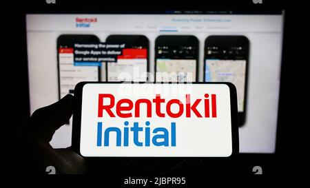 Personne tenant un téléphone portable avec le logo de la société britannique de services Rentokil initial plc à l'écran devant la page Web. Mise au point sur l'affichage du téléphone. Banque D'Images