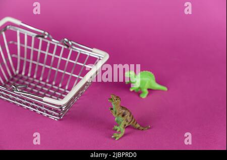 Dinosaures et un panier sur fond violet. Dinosaures se trouvant à côté d'un panier vide. Miniatures en plastique vert des animaux de proie Banque D'Images