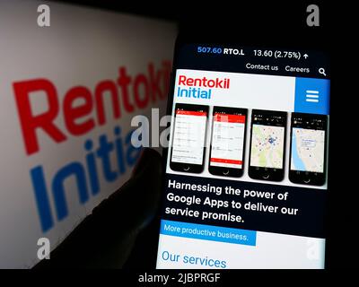 Personne tenant un téléphone portable avec la page web de la société britannique de services Rentokil initial plc à l'écran avec logo. Concentrez-vous sur le centre de l'écran du téléphone. Banque D'Images